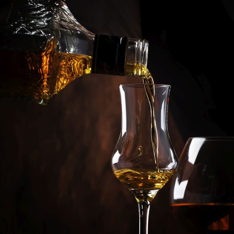 The bartender pours the liquor or brandy in glass on the old bar counter. Vintage wooden background in pub or bar, night mood. Place for text, toning, selective focus